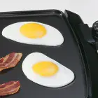 A close-up of fried eggs cooking on the 20-inch Cool-touch Electric Griddle.