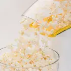 A close-up of popcorn flowing from the chute of the PopLite hot air popper and into a bowl.