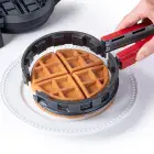 The Stuffler stuffed waffle maker's tongs being used to place a stuffed waffle on a plate..