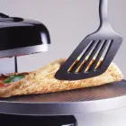 A close-up of the Pizzazz Plus rotating pizza oven with a spatula lifting the edge of a baking pizza to show the bottom of the crust.