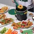 The Green and Gold FryDaddy electric deep fryer on a kitchen counter. The scoop is being used to remove a donut from the fryer and other deep fried foods are in the foreground.
