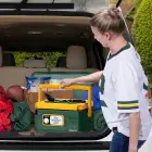 A woman putting the slow cooker in the back of an SUV.