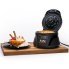 The Belgian Waffle Bowl Maker on a cutting board with the cover open and a waffle bowl on the cooking grid. A filled waffle bowl is on a plate to the left of the unit.