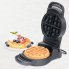 The Flip Belgian Waffle Maker with the cover open and a baked waffle on the cooking grid. A baked waffle is also on a plate in the background.