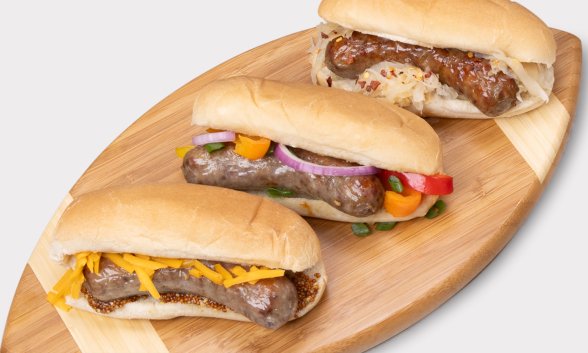 Three brats in buns on a cutting board.