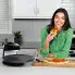 A woman enjoying pizza in a kitchen. The Pizzazz Plus rotating pizza oven is on the counter and a baked pizza is on a cutting board.