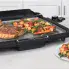 The Cool-touch Electric Griddle/Warmer Plus on a kitchen counter cooking steaks and vegetables..