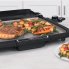 The Cool-touch Electric Griddle/Warmer Plus on a kitchen counter cooking steaks and vegetables..